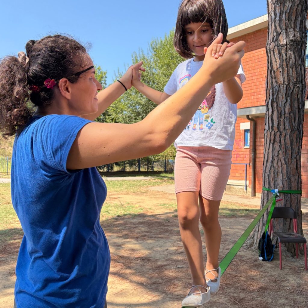 professionista di Contesto che accompagna una bambina nel gioco della slack-line durante il centro estivo 2026